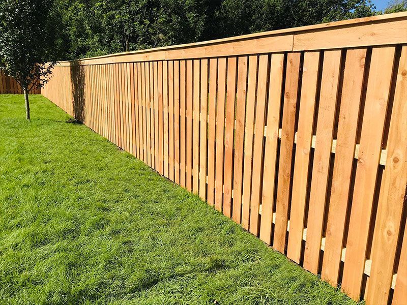 A tall wooden privacy fence stands alongside a green grassy lawn in an outdoor setting.