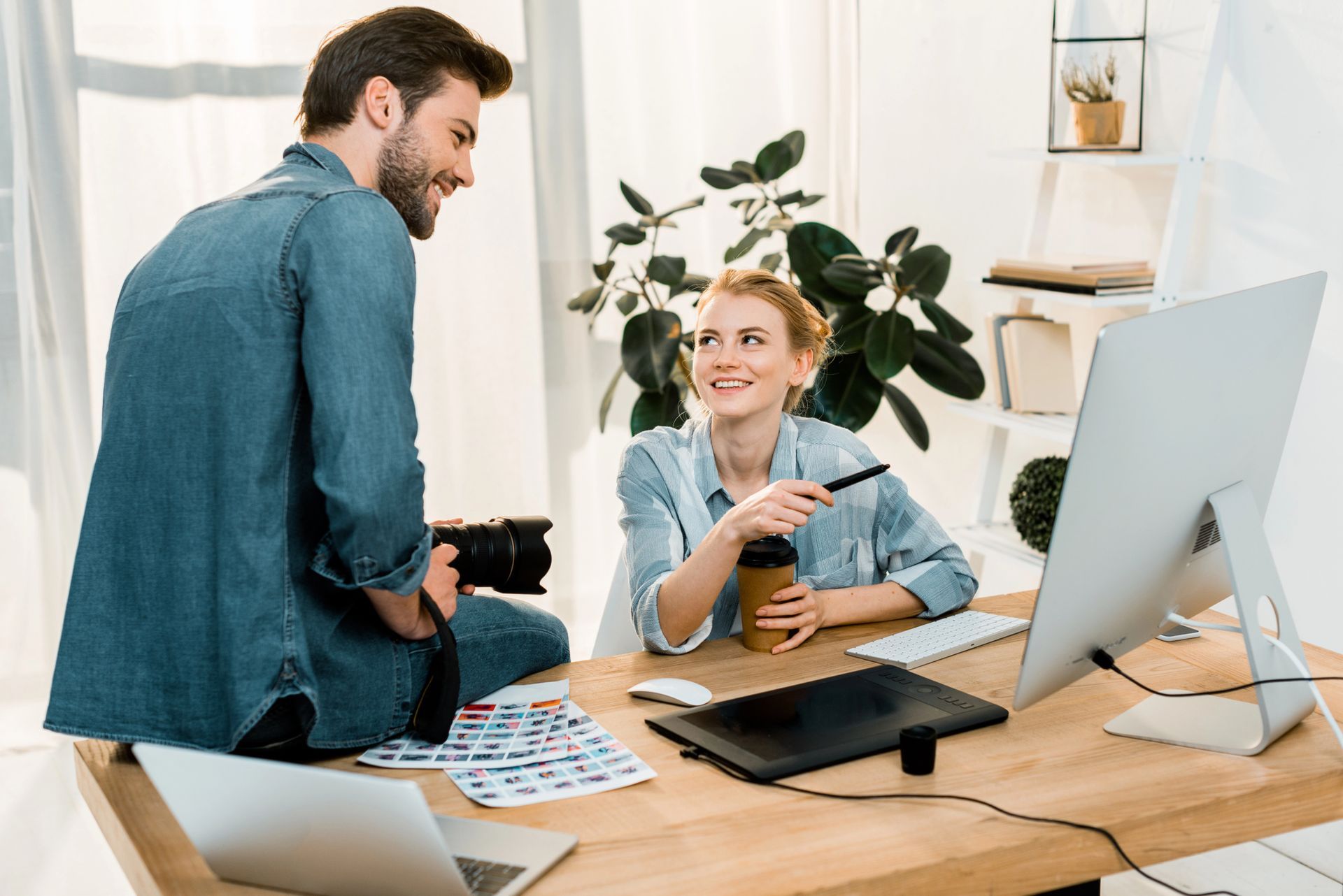 Hombre con cámara y mujer con lápiz mirando la computadora en la oficina.