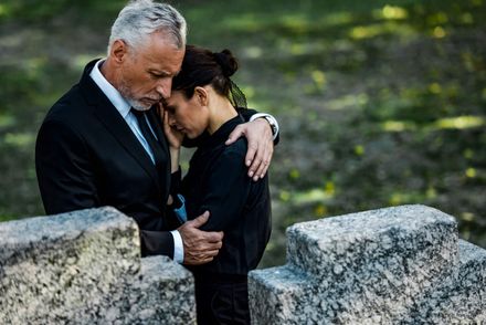 Two people embracing in a cemetery, one consoling the other among stone graves.