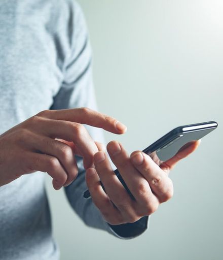 Person using a smartphone with both hands against a light gray background
