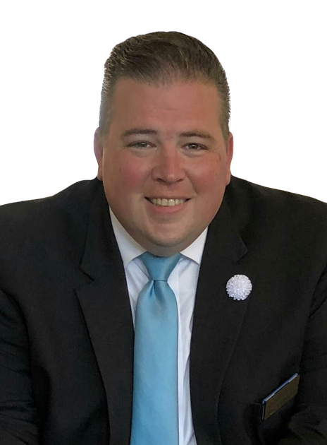 Portrait of a smiling man in a black suit with a light blue tie and white lapel pin on a white background