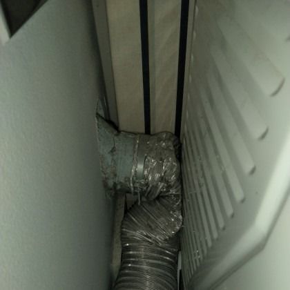 Flexible ducting squeezed between two white panels in a narrow gap.
