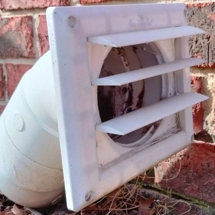 White wall vent with louvered grate and duct pipe mounted on a brick exterior wall