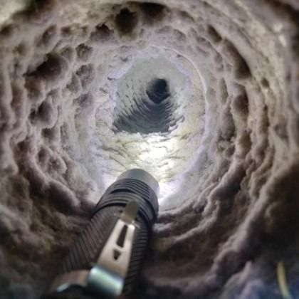 Inside a snowy tunnel, a flashlight points toward the bright opening above.