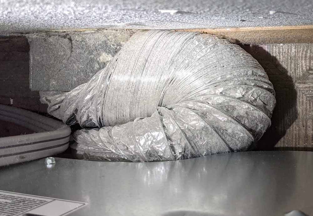 Silver insulated HVAC duct inside a wall cavity above a metal panel