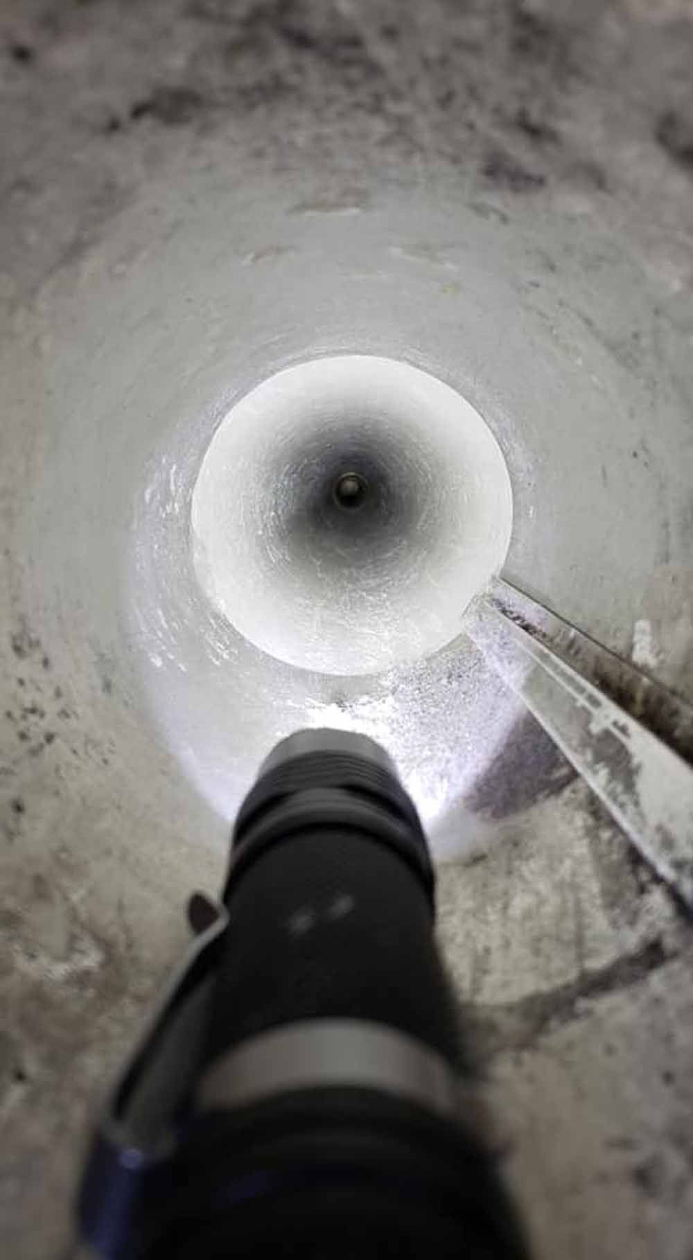 Inside a concrete pipe, a flashlight illuminates the tunnel while a metal tool points toward the center.