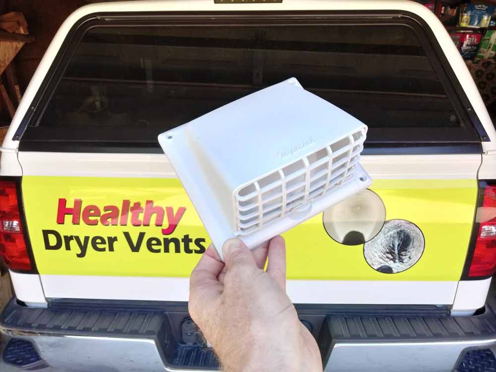 Hand holding a white dryer vent cover in front of a truck with “Healthy Dryer Vents” sign