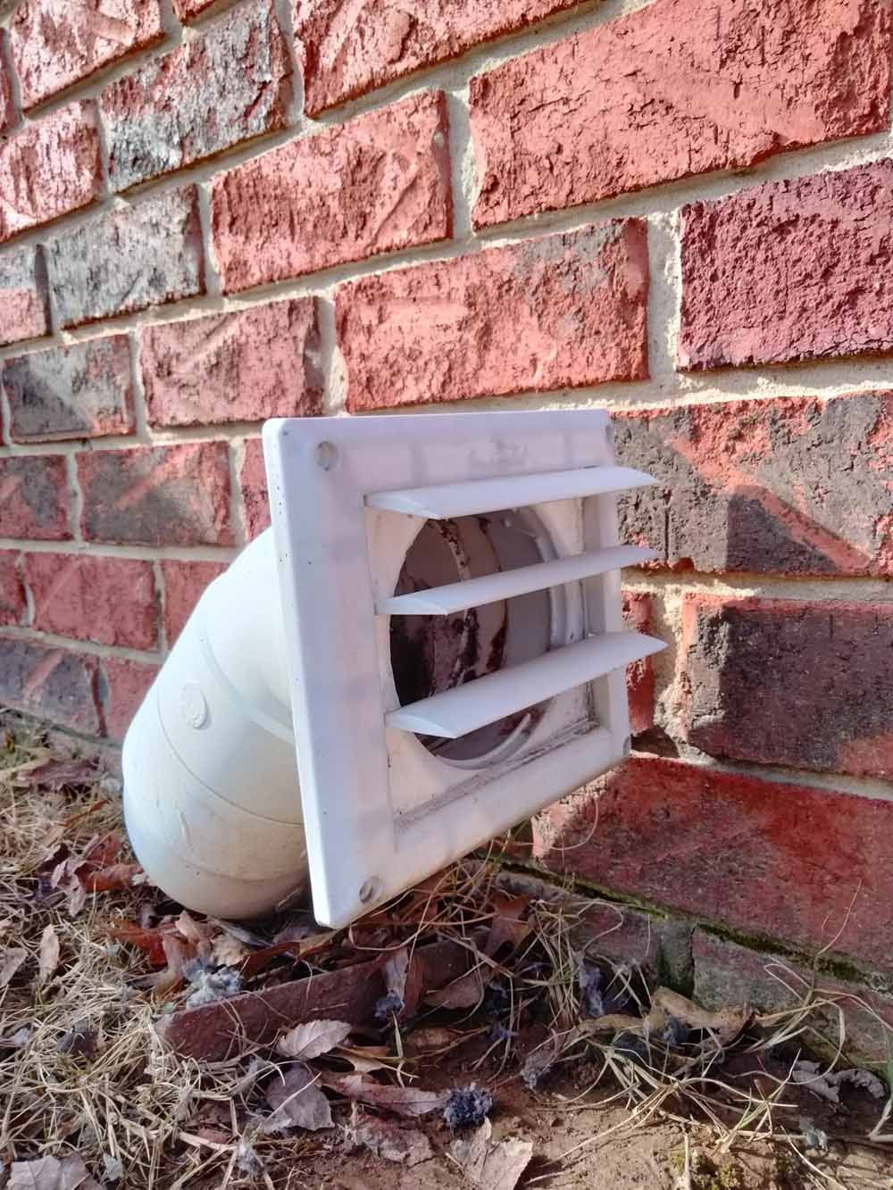 White vent pipe with louvered cap against a red brick wall outdoors