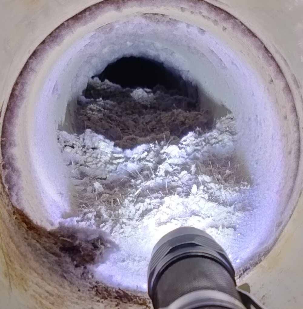 Inside a round pipe, white residue lines the walls as a flashlight illuminates debris ahead.