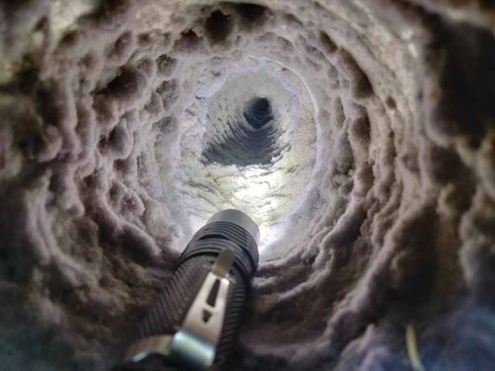 Looking up inside a dirty pipe with a flashlight shining upward toward the opening