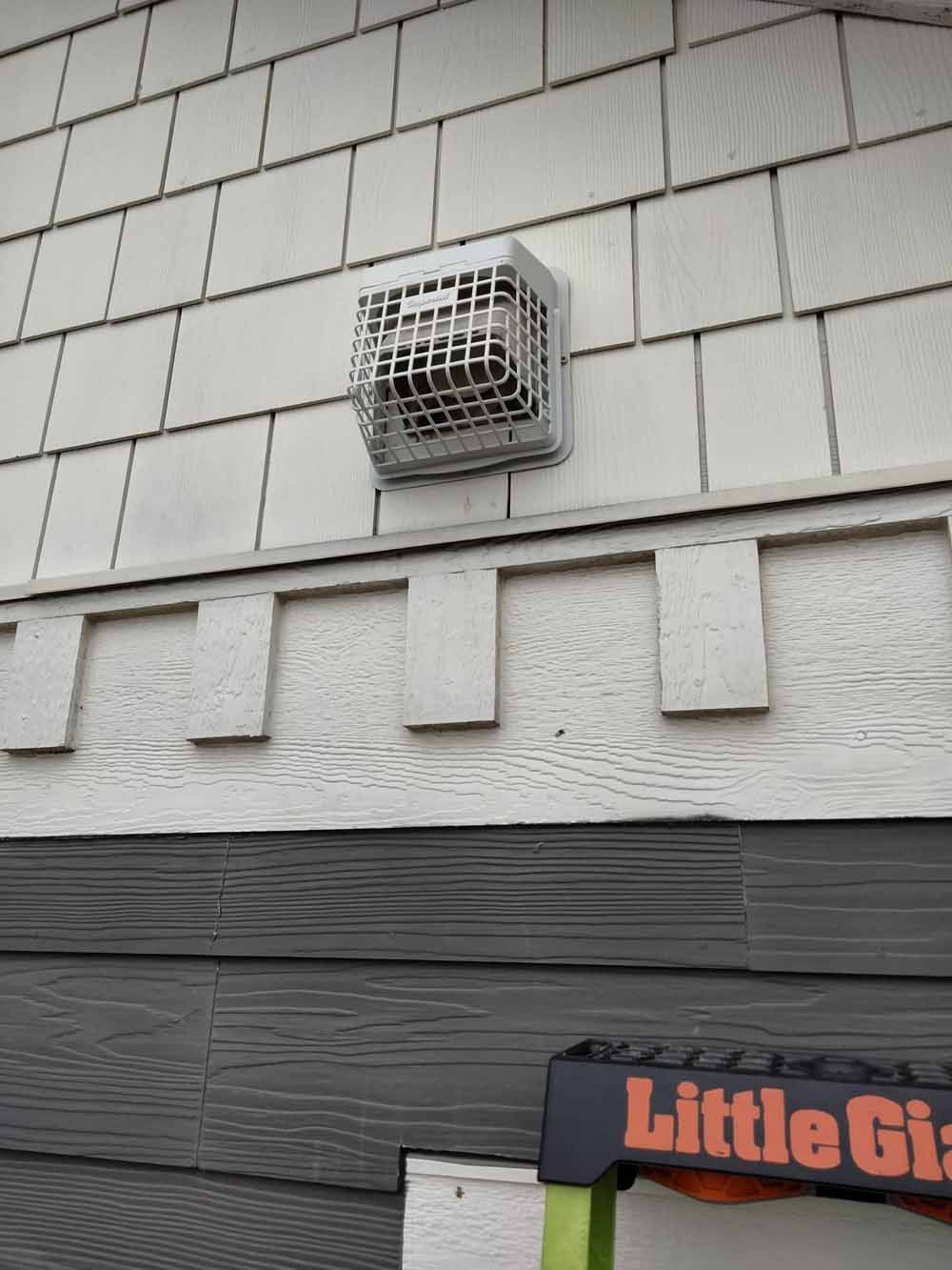 Exterior wall with a small white vent above gray siding and a partial Little Caesars sign below