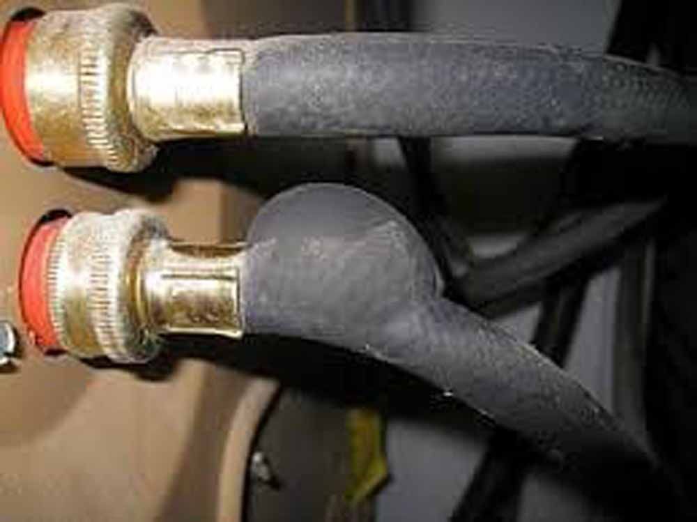 Close-up of two black hoses connected to brass fittings with red rings