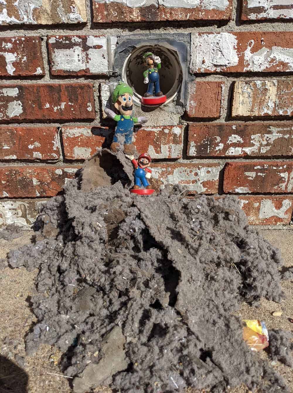Three small toys on a mound of gray lint against a brick wall, with a round reflective object above.