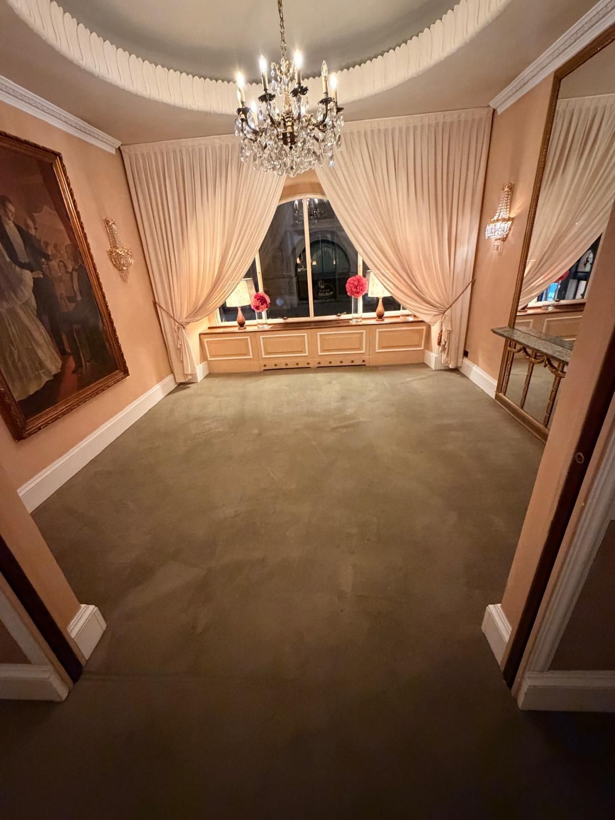 Sala da pranzo formale vuota con moquette beige, lampadario, finestra con tende e armadi a muro.