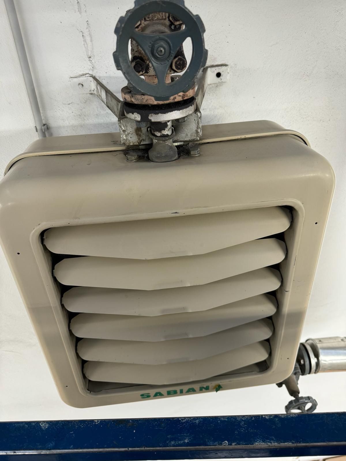 Bocchetta di ventilazione beige fissata alla parete, con lamelle e una maniglia blu della valvola sopra, con segni di ruggine e usura