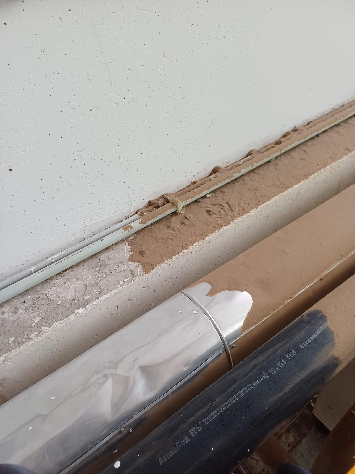 Battiscopa danneggiato con vernice scrostata e un tubo o cavo bianco che corre lungo il muro.