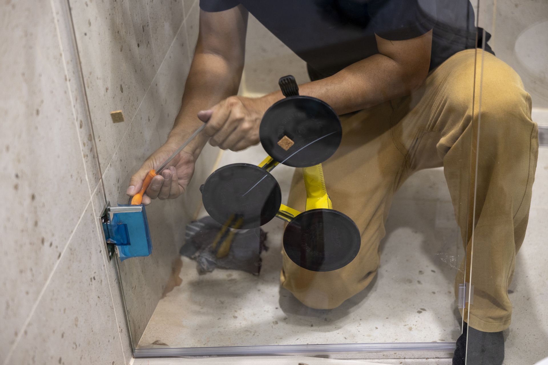 Worker installing a blue electrical box in a concrete wall with a suction-cup tile cutter nearby.
