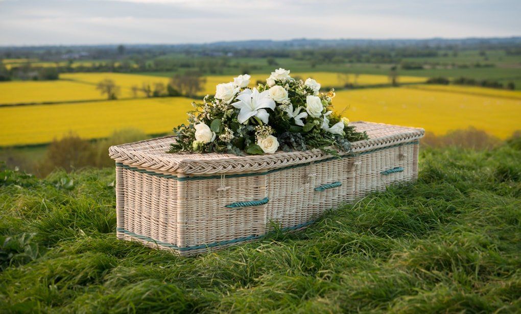 Wicker coffin topped with flowers in a countryside setting
