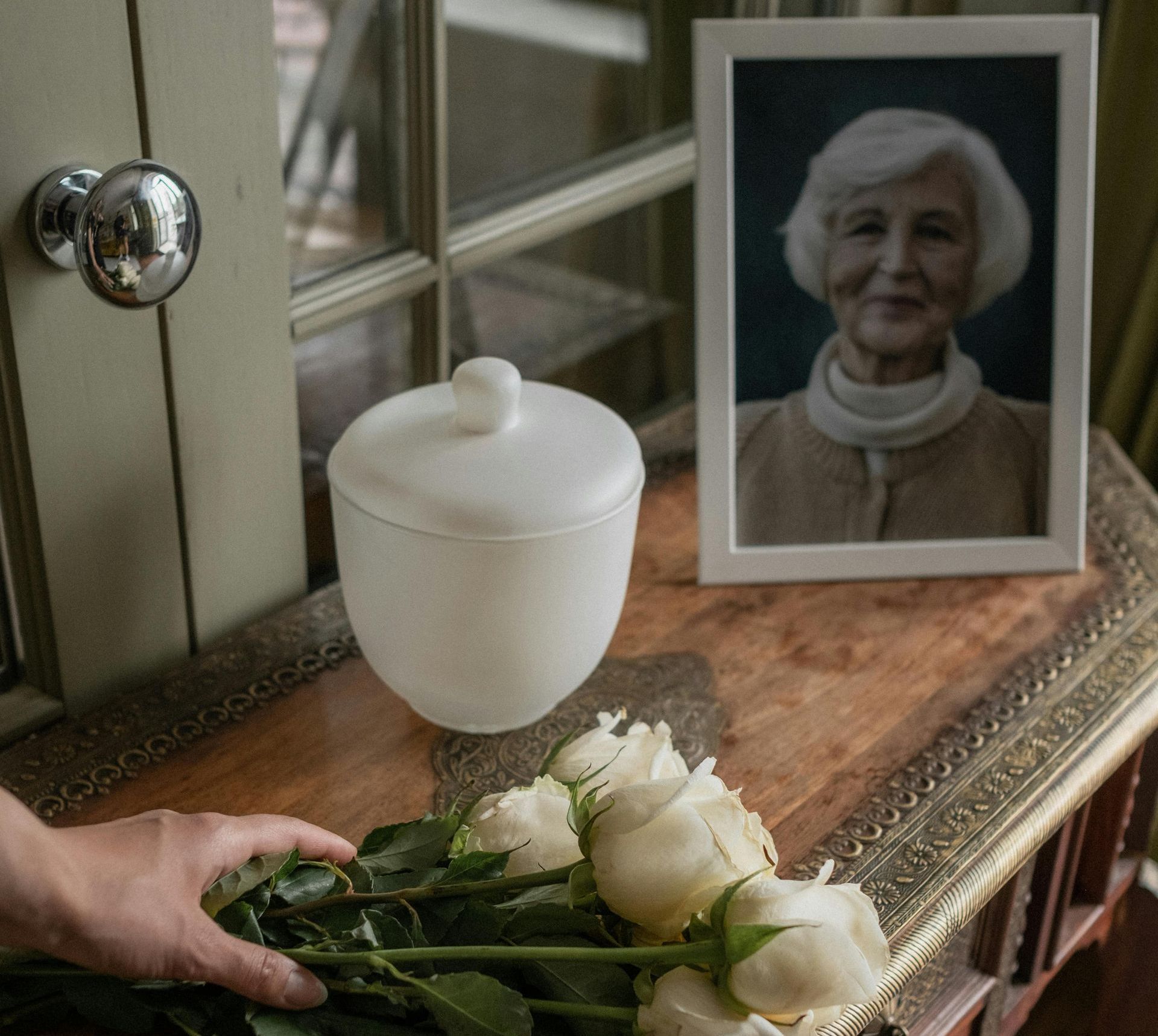 Framed photo of an old woman next to an urn and a hand holding some flowers