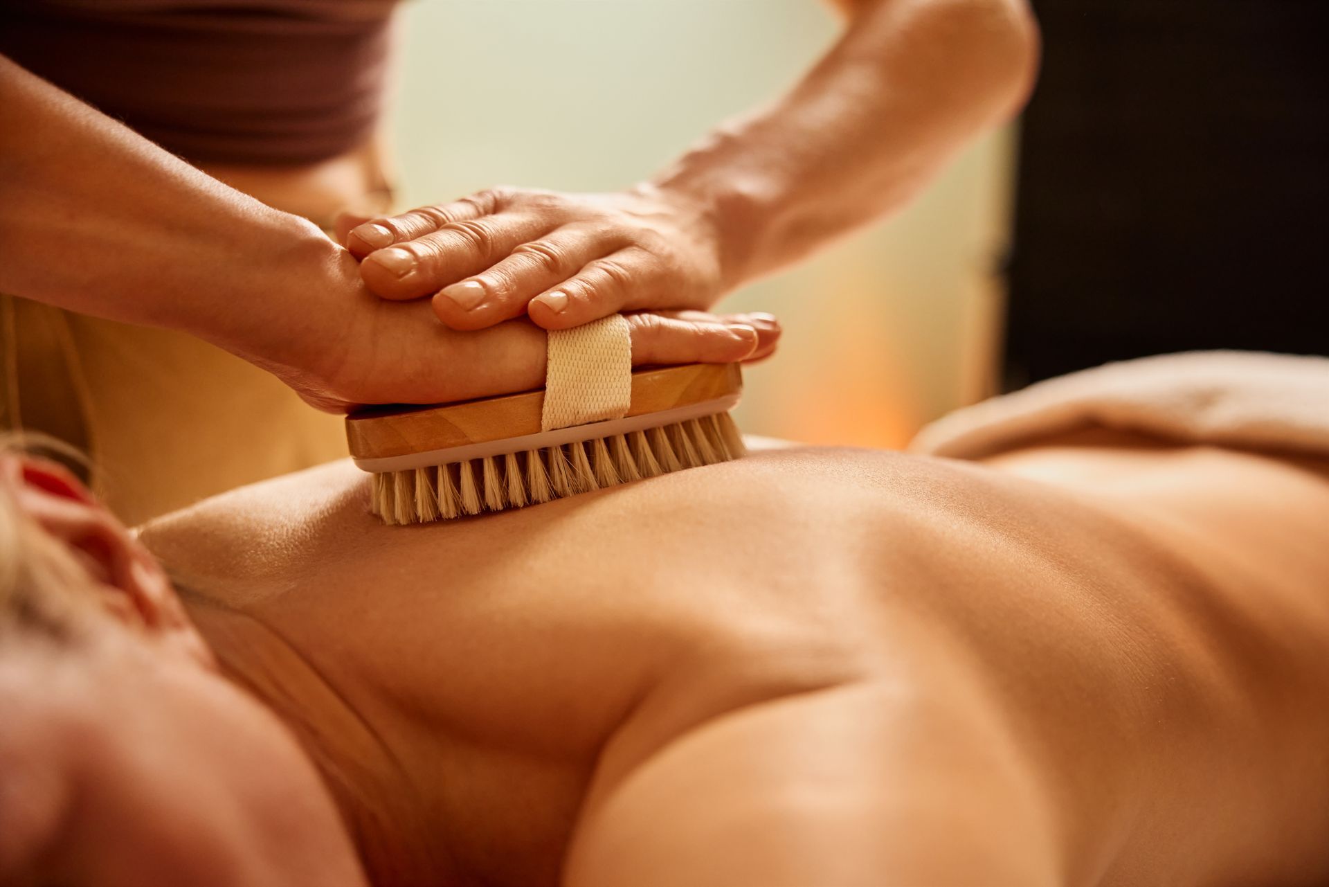 Massage therapist using a brush on a person’s back in a spa setting Massage therapist using a brush on a person’s back in a spa setting