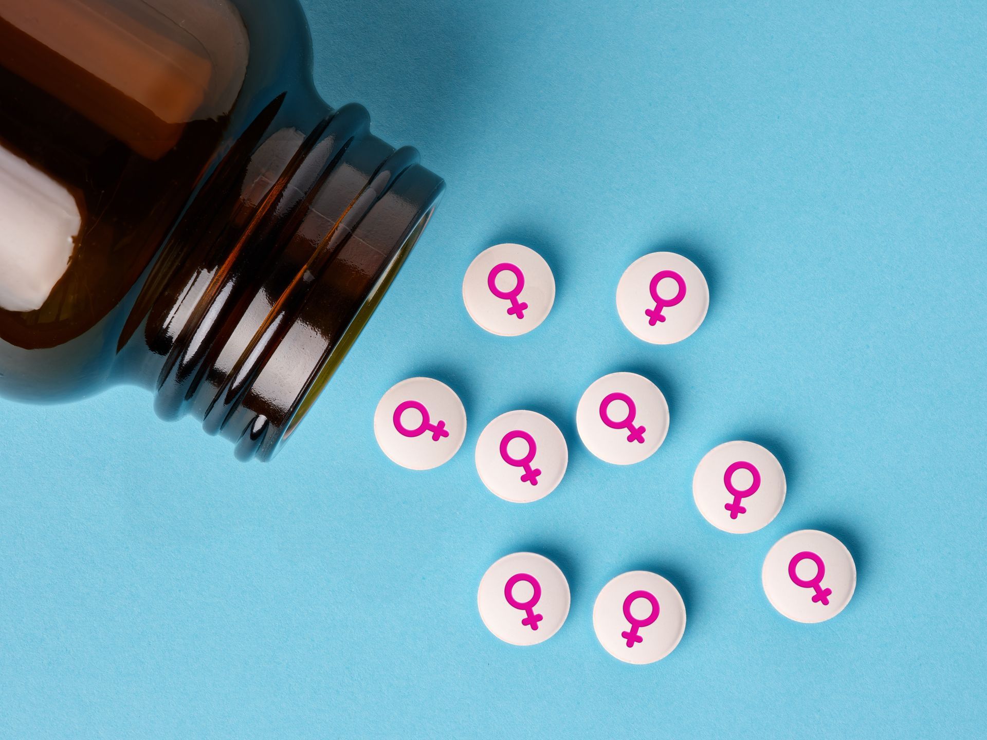 Pill bottle spilling pink female-symbol tablets on a blue background Pill bottle spilling pink female-symbol tablets on a blue background