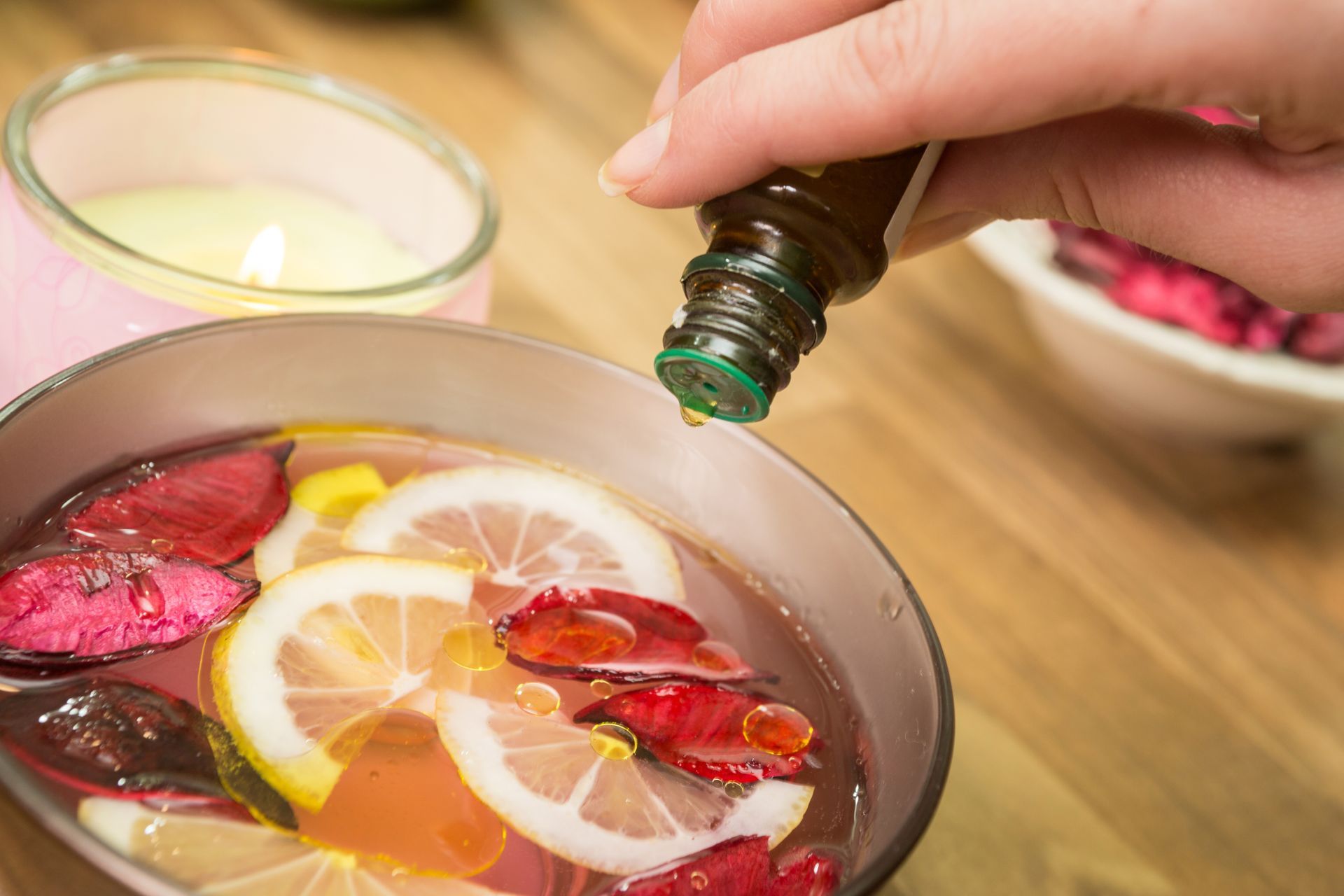 Hand pouring green liquid into a bowl with floating lemon slices and red petals Hand pouring green liquid into a bowl with floating lemon slices and red petals