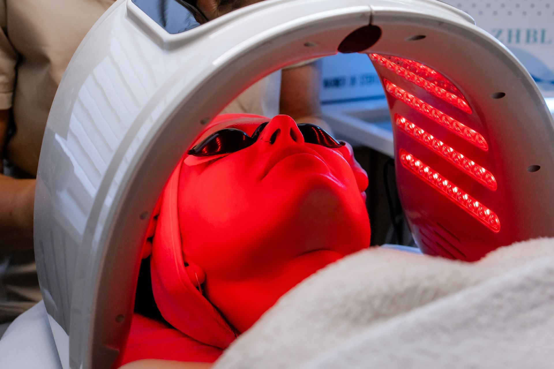 Person wearing sunglasses under red LED light therapy panel