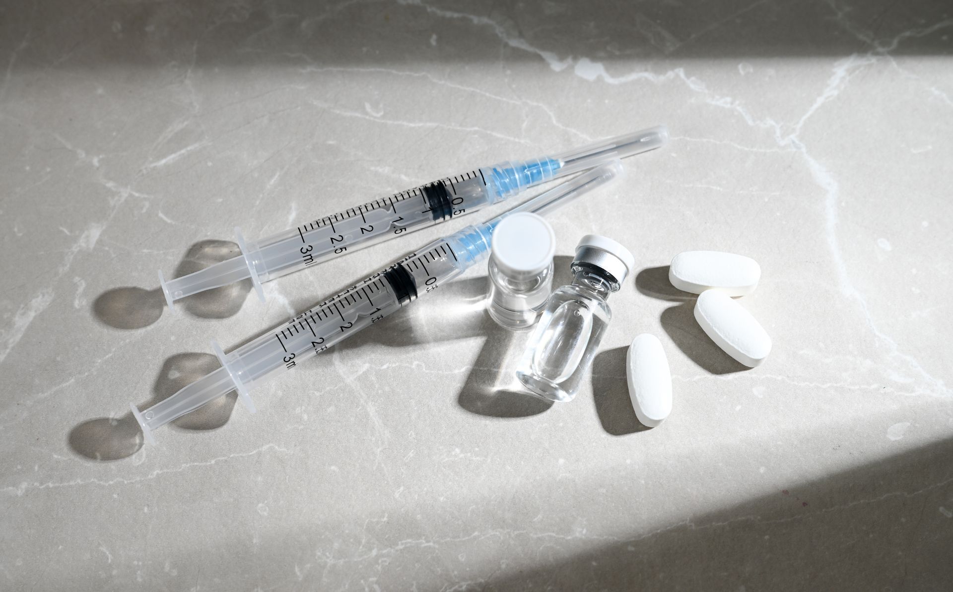 Syringes, vials, and white pills on a sunlit surface