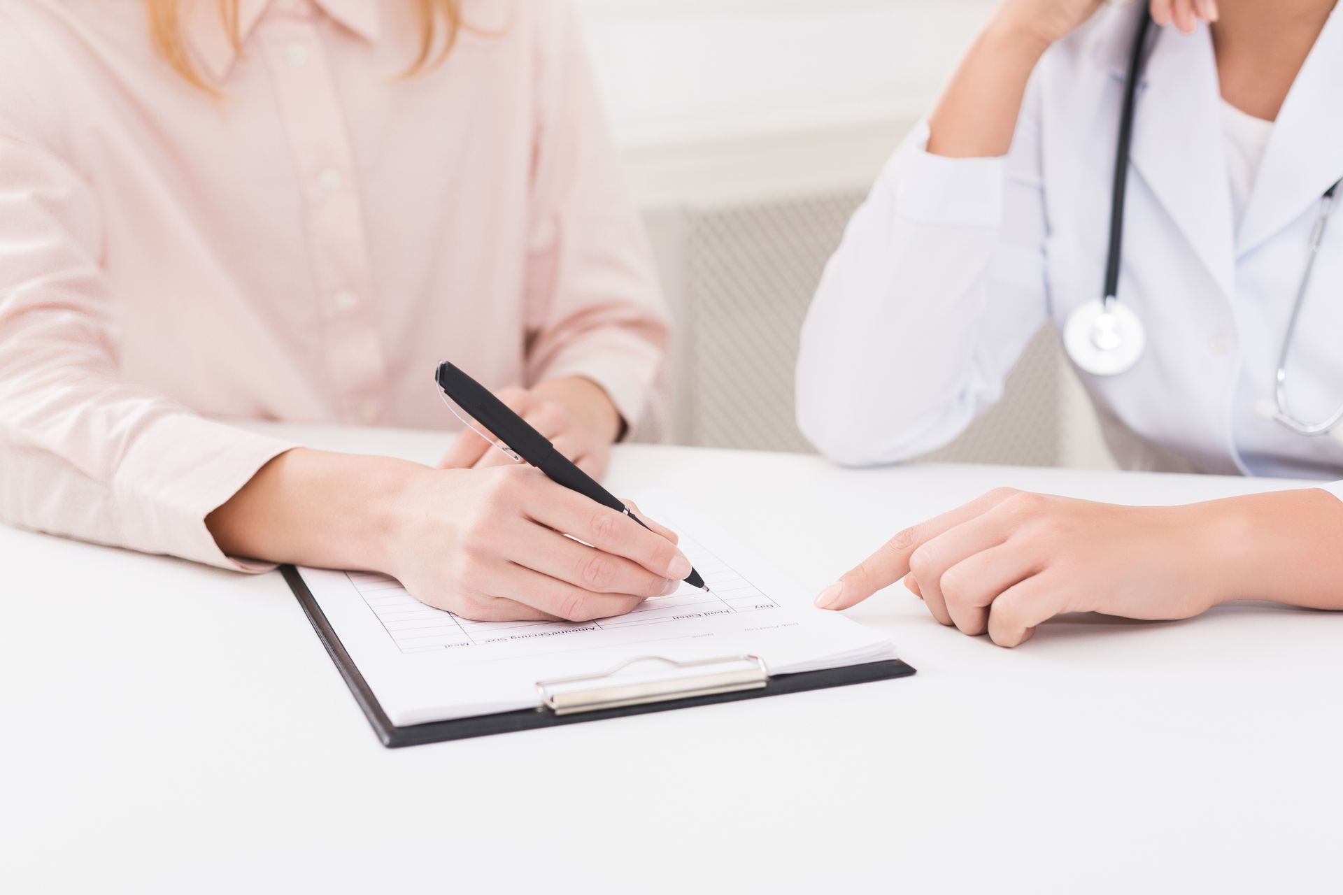 Two people in a medical consultation, one writing on a clipboard at a desk
