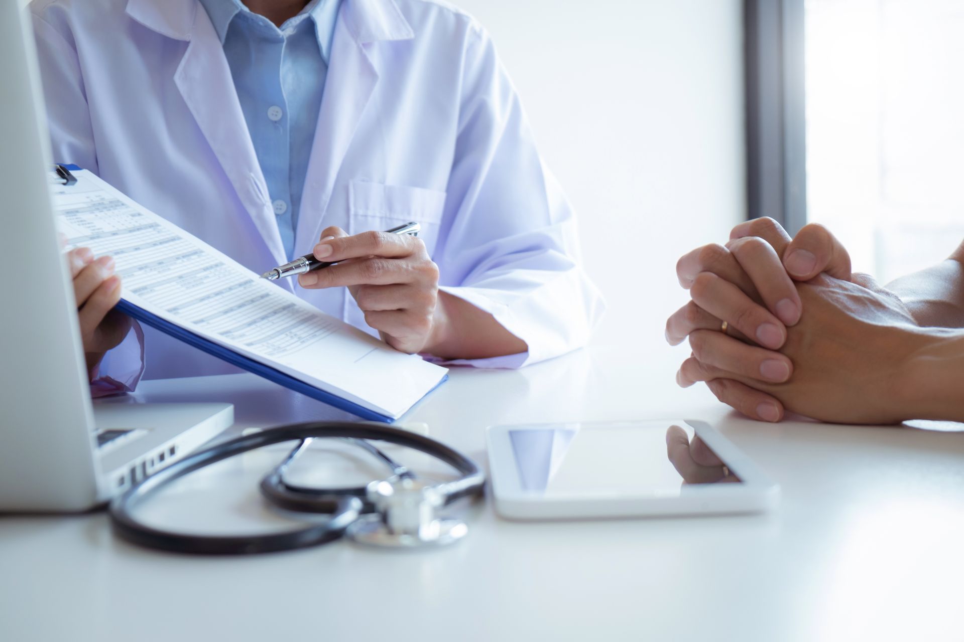 Doctor taking notes during a consultation with a patient, stethoscope and tablet on the desk