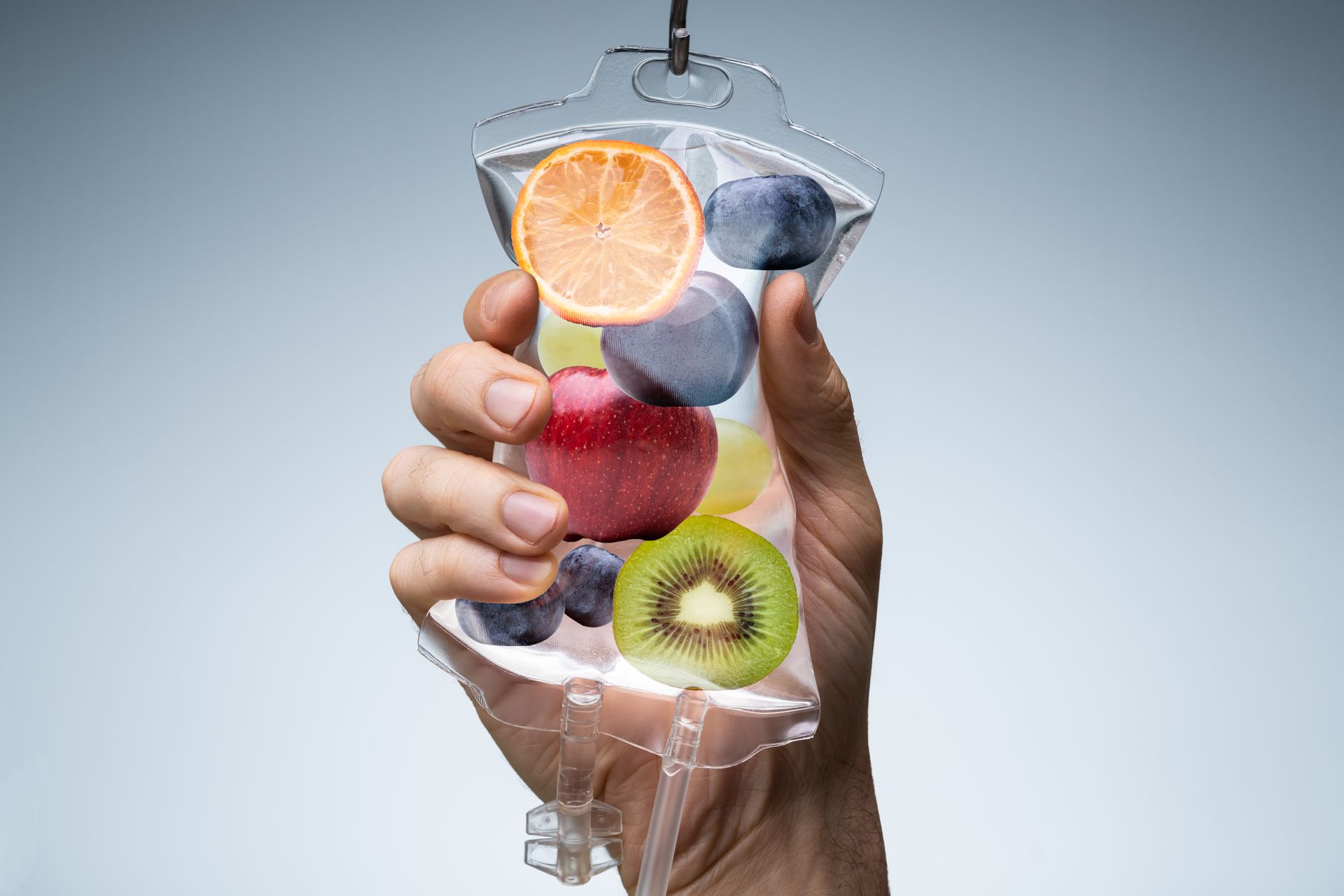 Hand holding a clear plastic bottle filled with mixed fruit slices and water