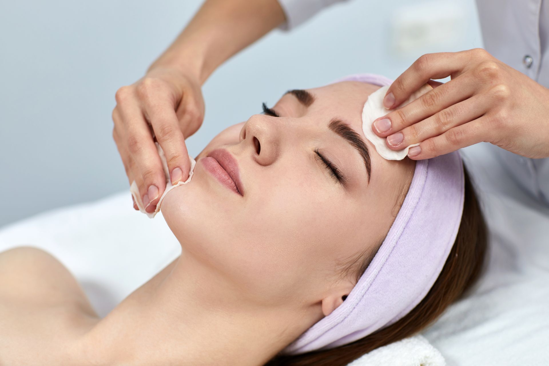 Spa facial treatment with hands applying cream to a woman’s face using cotton pads