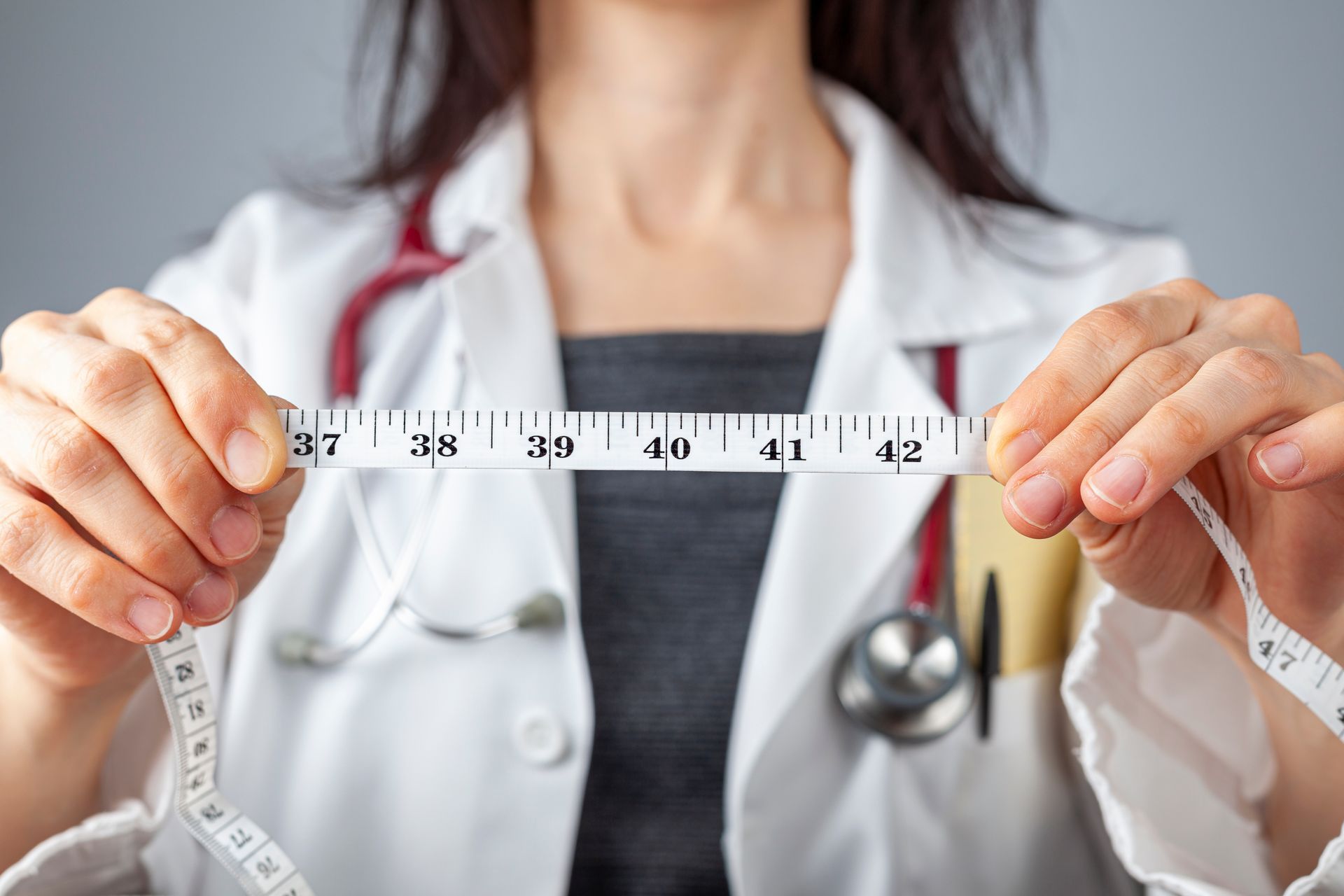 Close up isolated image of a caucasian doctor holding a tape measure in her hands which shows 40 inches as abdominal circumference upper limit in healthy people.