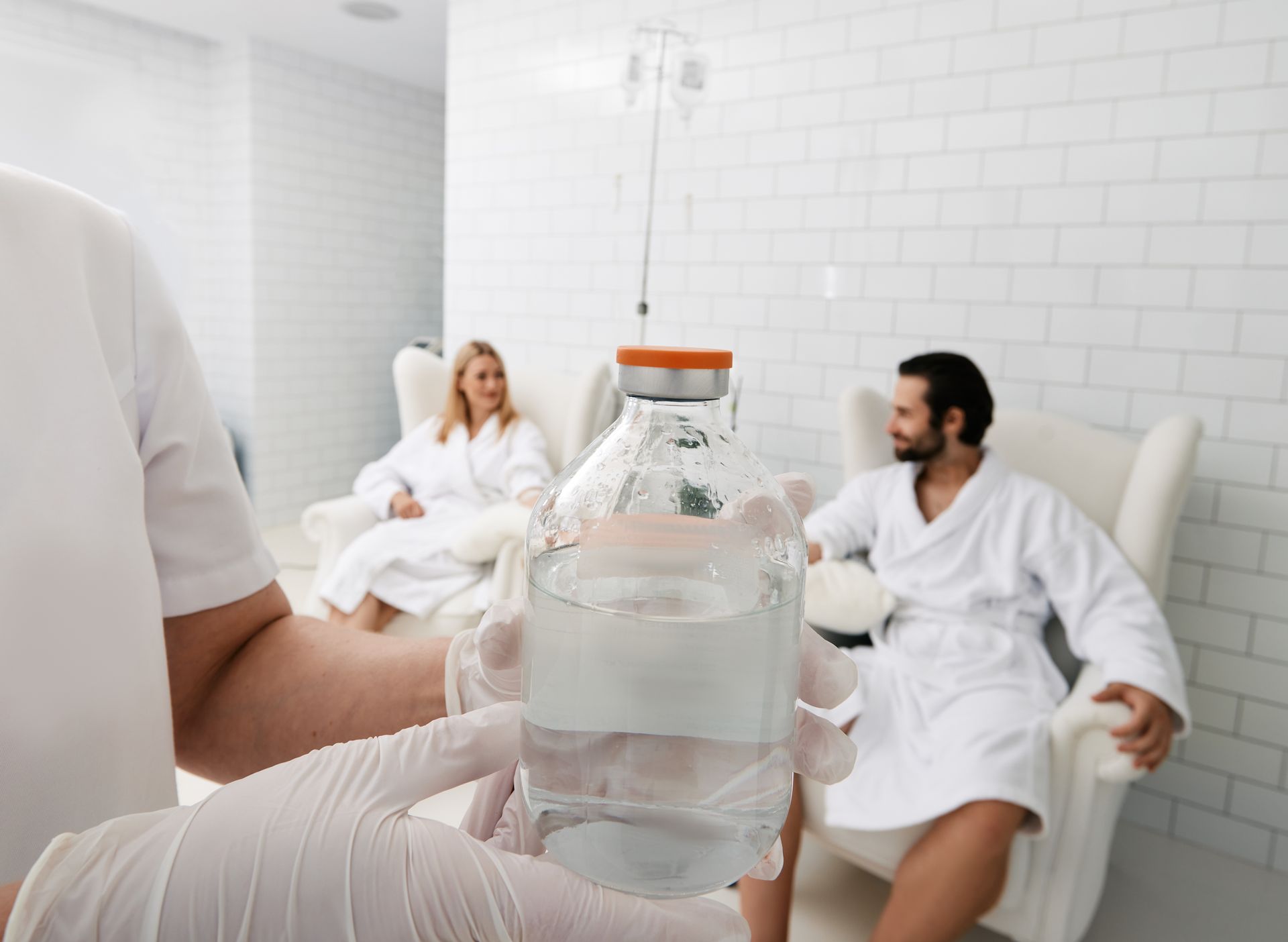 Water bottle in foreground, with two people in white robes relaxing in a bright spa lounge