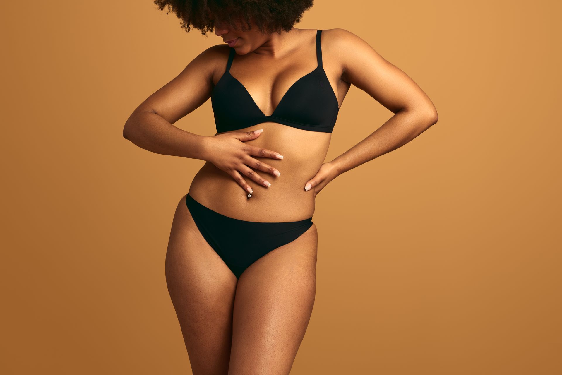 Woman in black bikini posing against a warm brown background.