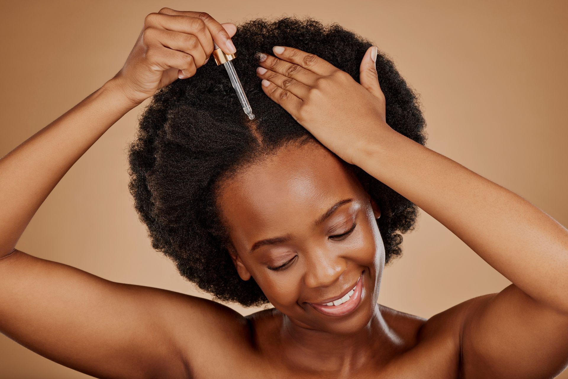 Person applying hair treatment to natural hair, smiling against a warm brown background