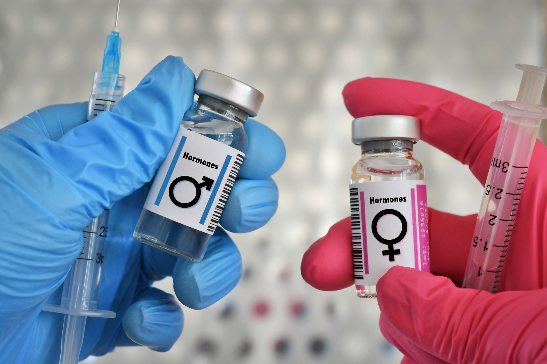 Gloved hands holding male and female hormone vials next to syringes in a lab setting