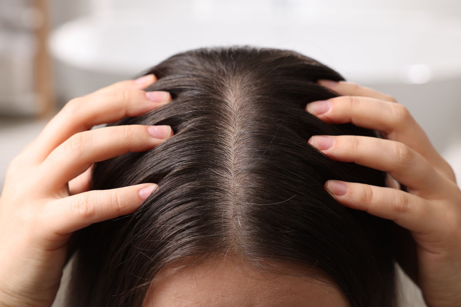 Hands parting dark hair along a center part on the scalp