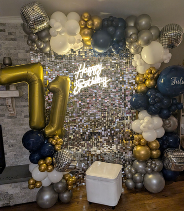 Party decorations with balloons, wood stumps, and a green cabinet in a grassy outdoor setting.