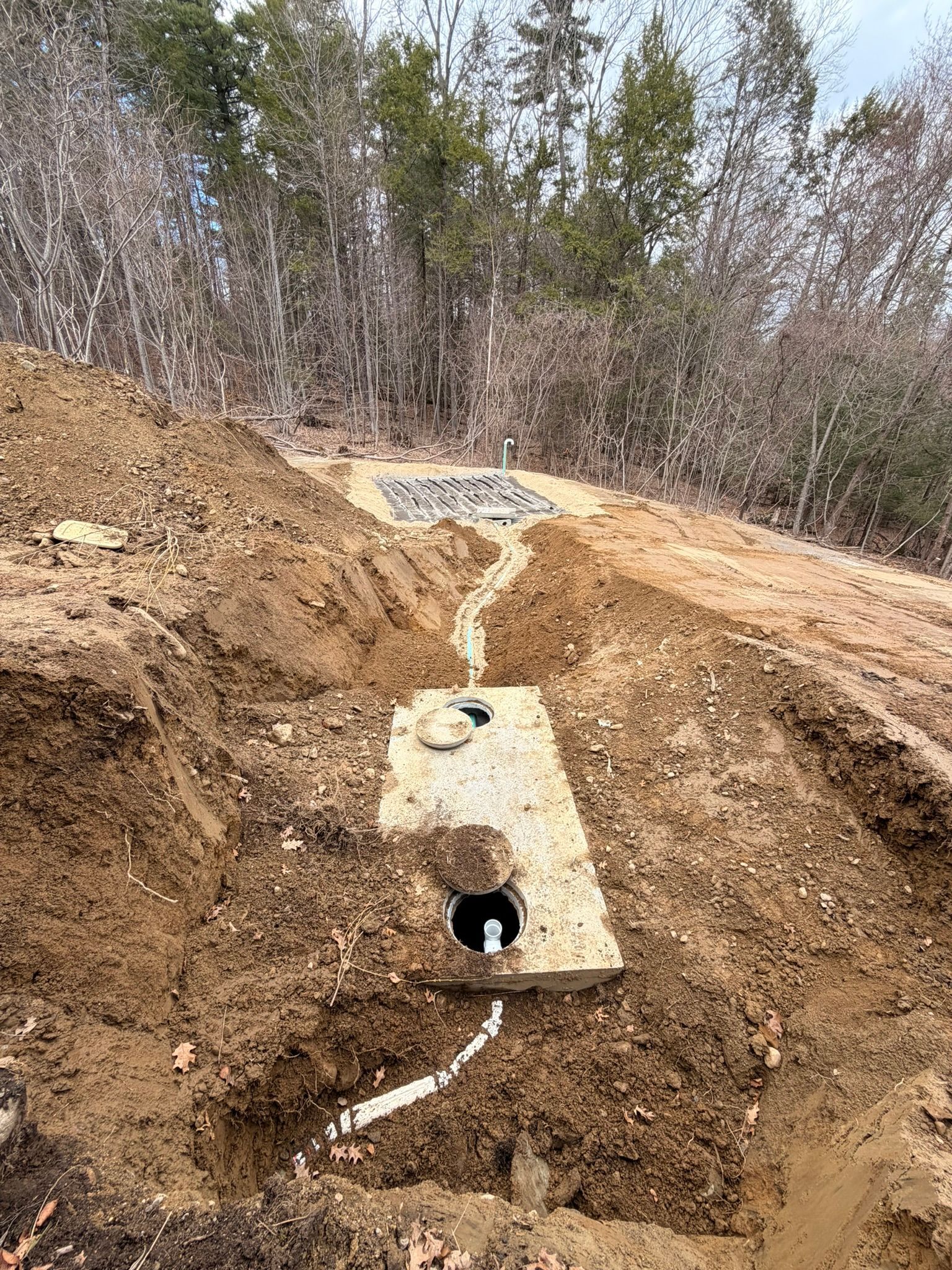 Dirt trench with a concrete pipe and drainage channel in a wooded construction site