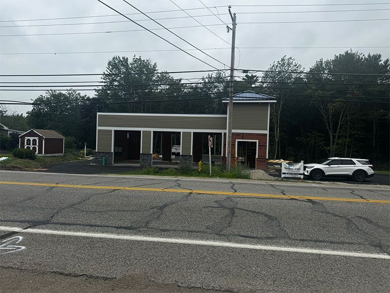 Building under construction with open bays on a road. A white SUV is parked in front.