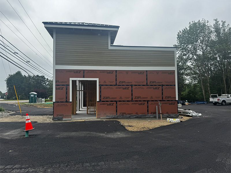Building under construction, brown siding, open doorway, green roof section, black asphalt, outdoor setting.