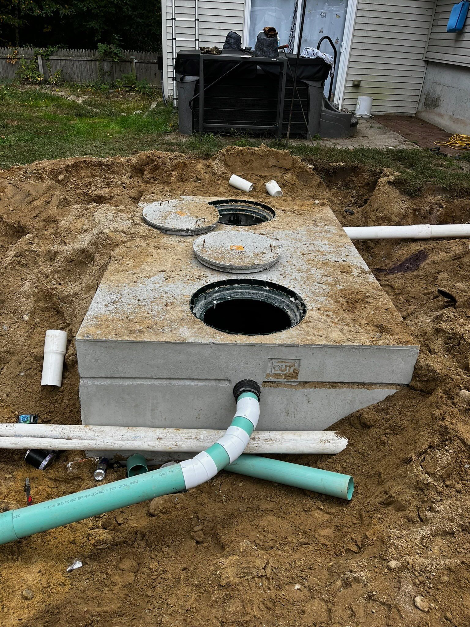 Concrete septic tank installation with open access points and connecting pipes in a yard.