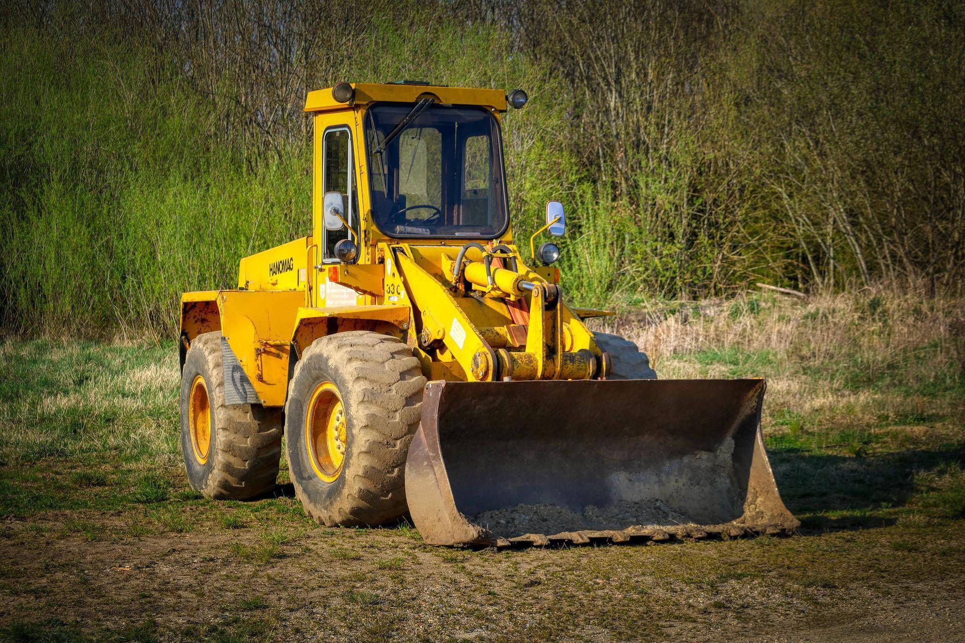 Yellow bulldozer parked on brown ground, with green foliage in the background.