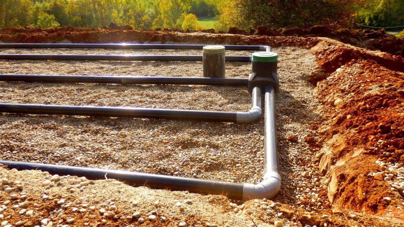 Underground irrigation system with black pipes laid in gravel, connected to a green and gray control valve.