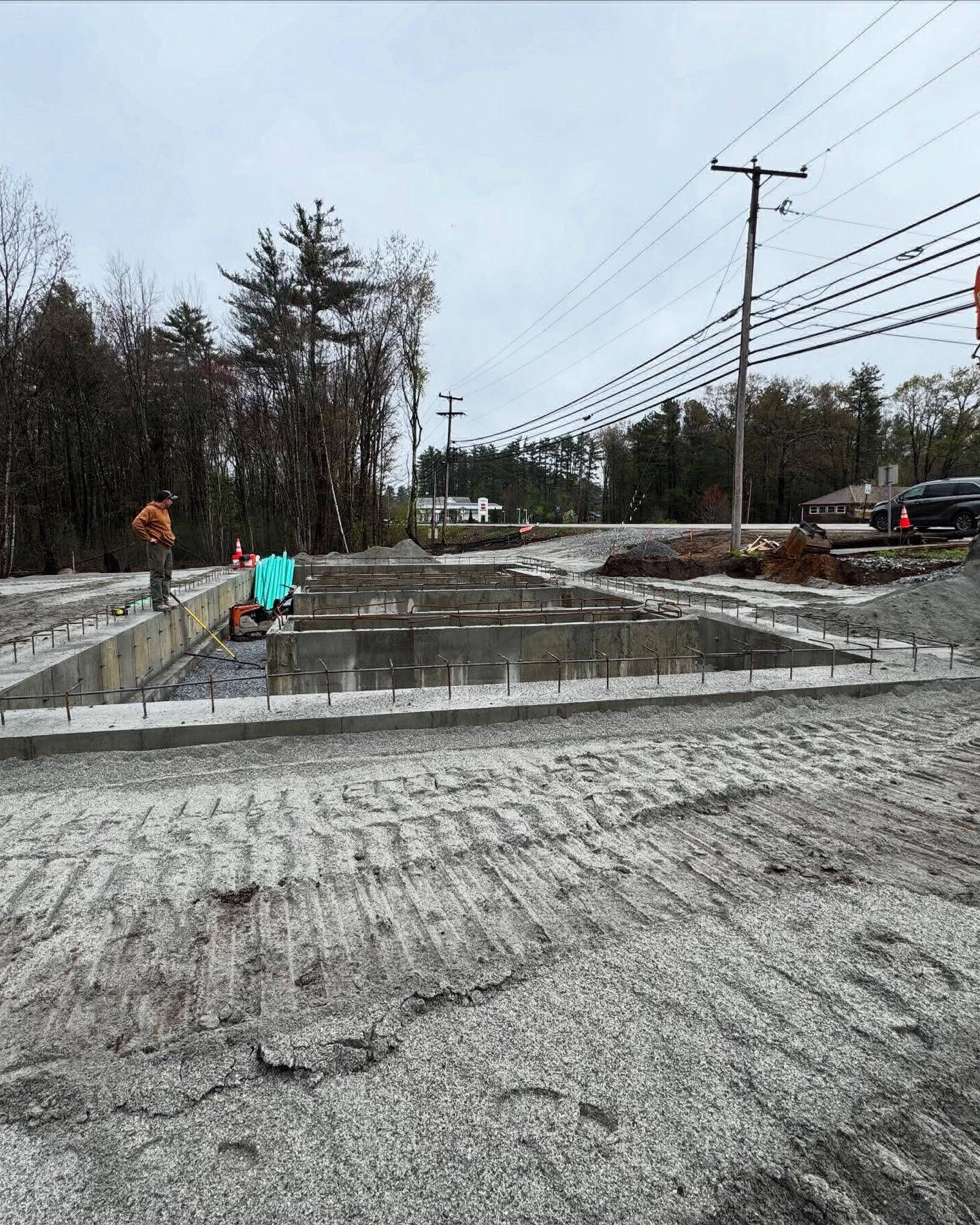 Construction site with concrete foundation and gravel ground under overcast sky.