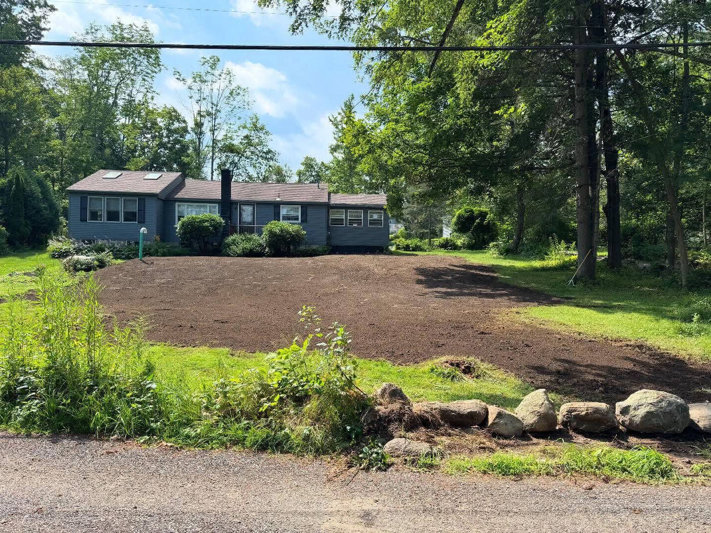 Blue house with freshly tilled yard, framed by trees and a gravel road.
