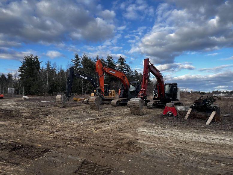 Three excavators on a construction site under a cloudy sky.