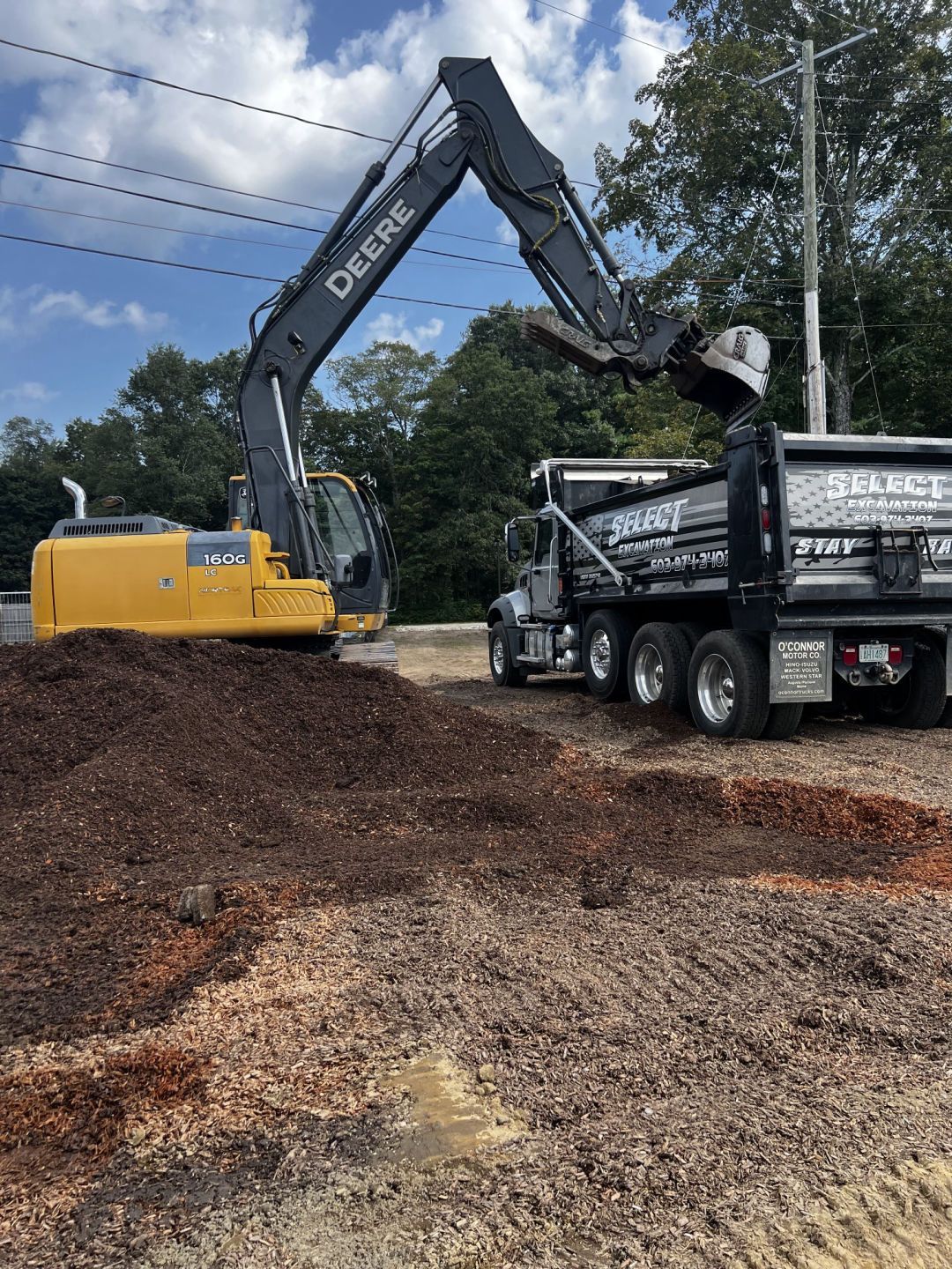 A John Deere excavator loads a black dump truck with dirt on a construction site.