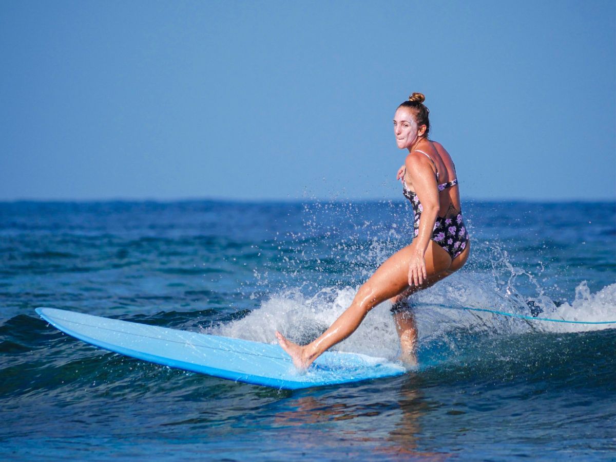 Surfer riding a blue surfboard on small ocean waves under a clear sky